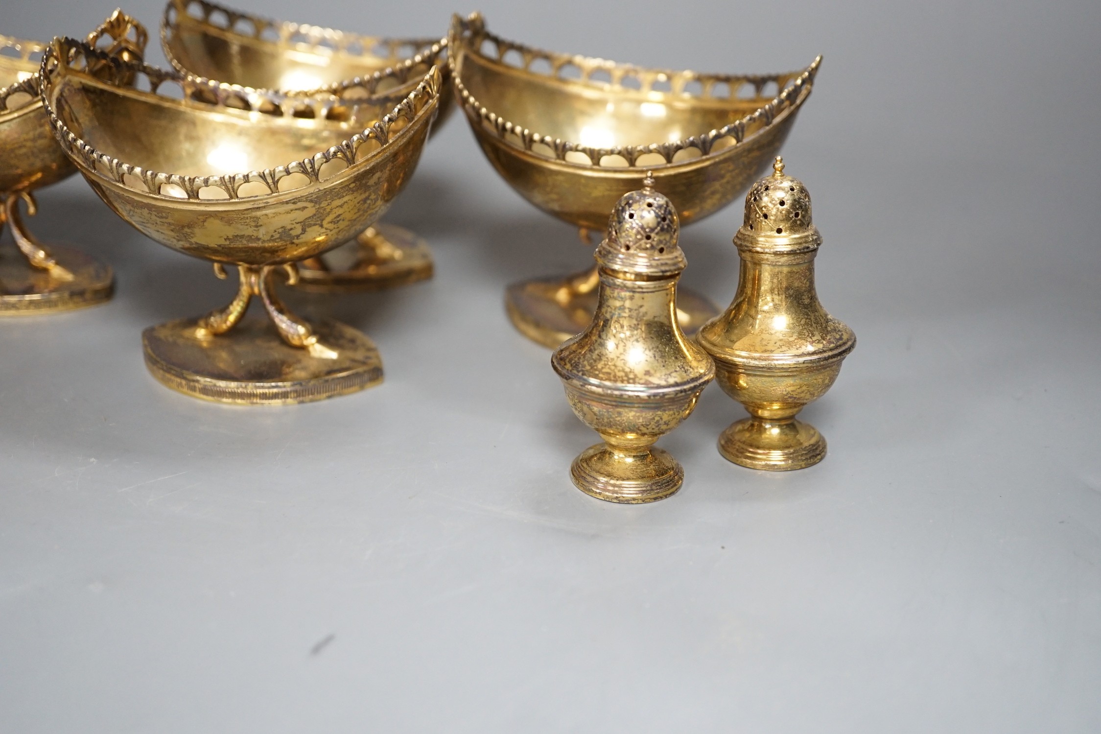 A set of four 20th century Spanish gilt white metal boat shaped pedestal bowls, with pierced borders, on twin dolphin supports 10.3cm and a set of four similar pepperettes, 18oz.